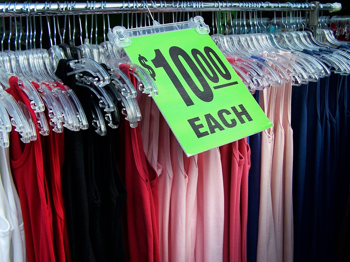 A packed clothing rack of tank tops with a neon green ten dollars each sale sign clipped to the rail
