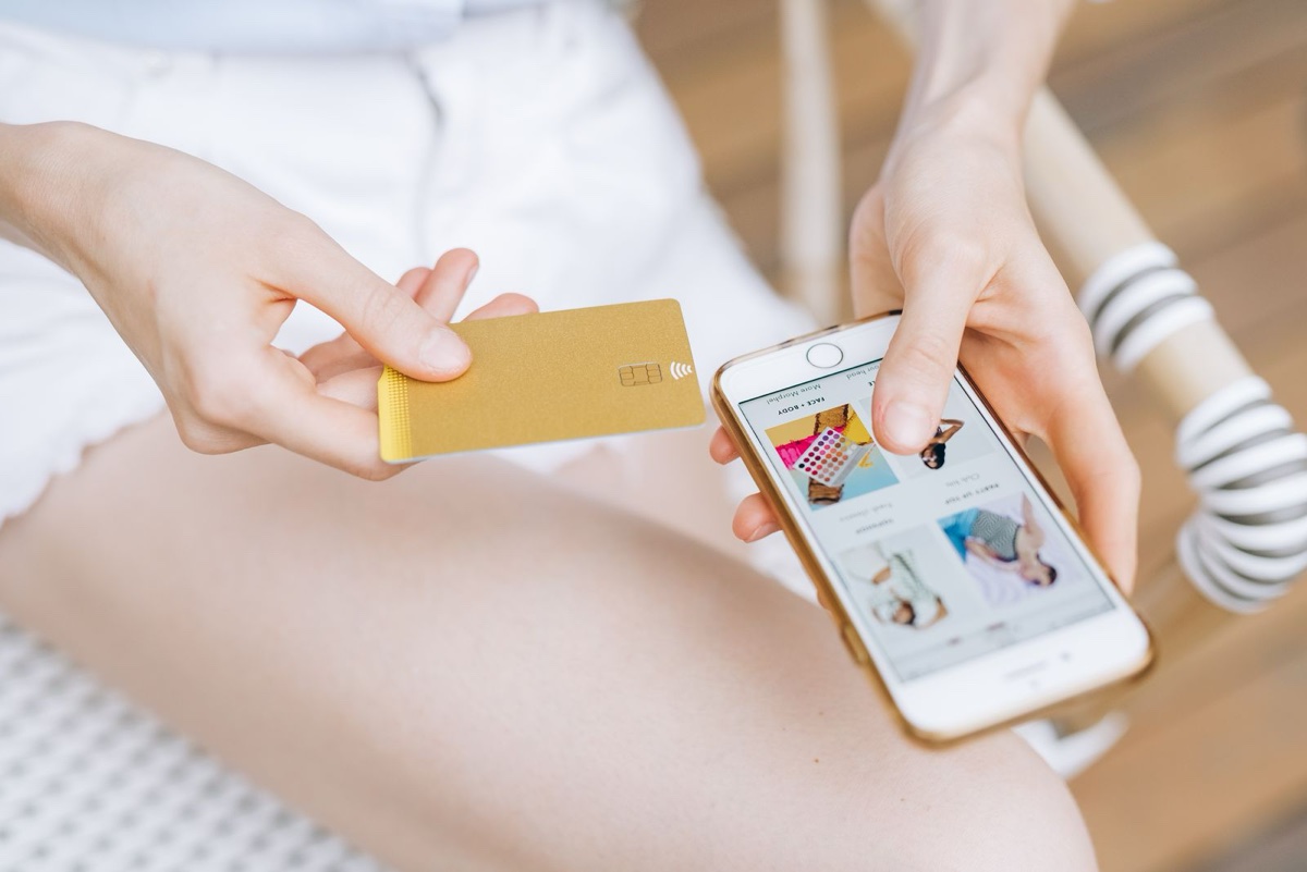 Close-up of hands holding a gold payment card and a phone showing a shopping app