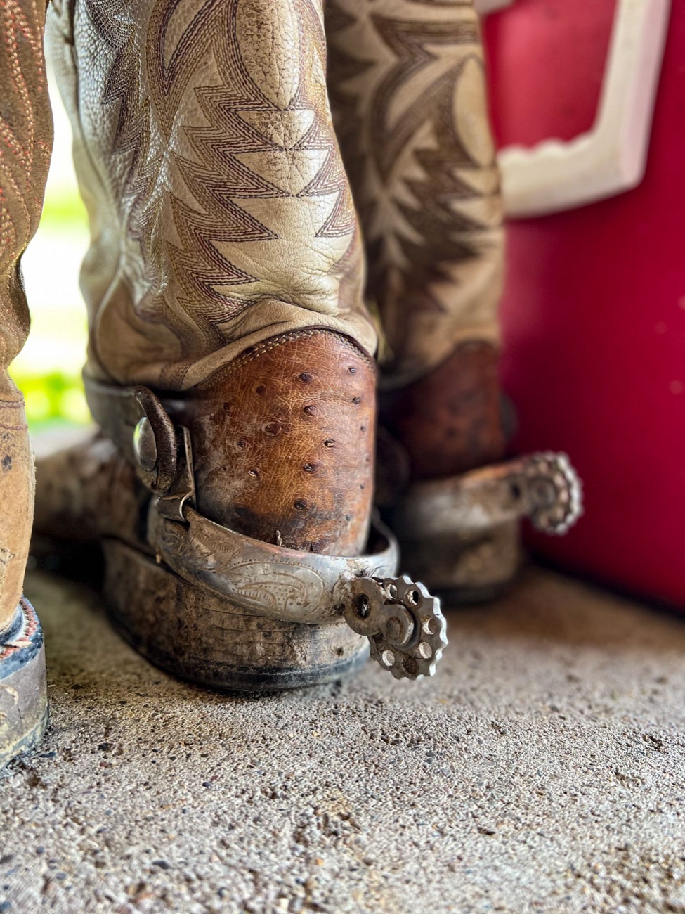 Close-up of two worn cowboy boot heels with engraved spurs, the leather scuffed and the heel edges rounded from wear
