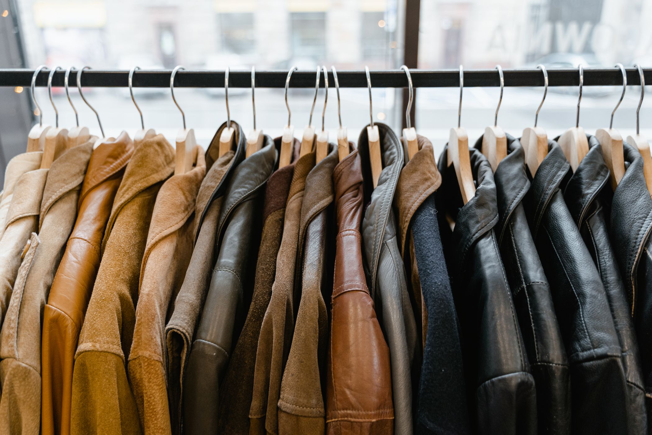A rack of leather and suede jackets on wooden hangers in front of a shop window