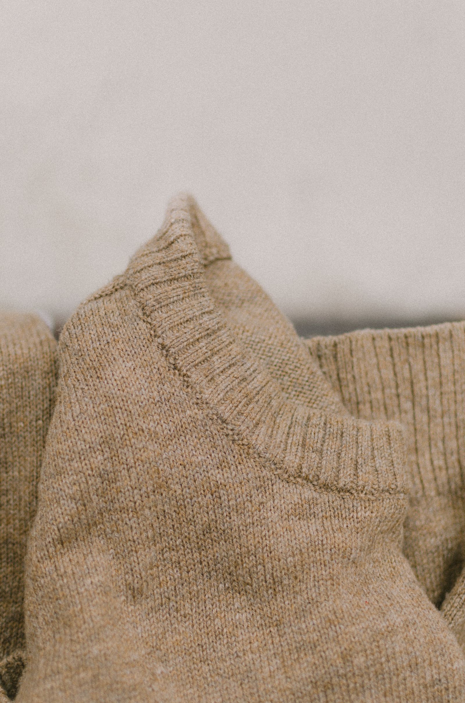 Close-up of a camel knitted crewneck sweater collar showing ribbed trim and jersey stitch texture