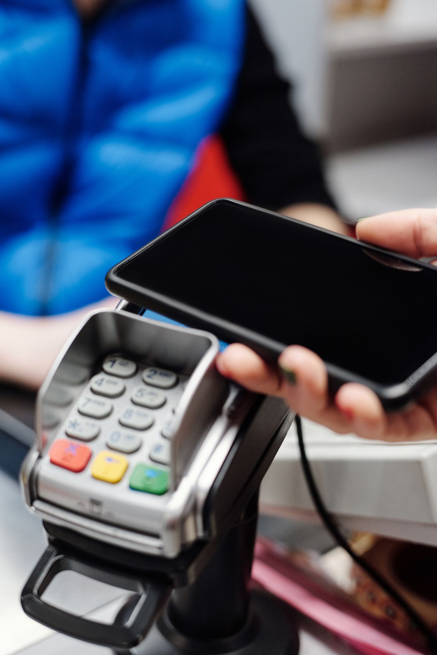 A hand with green nail polish holding a smartphone over a card terminal at a store counter