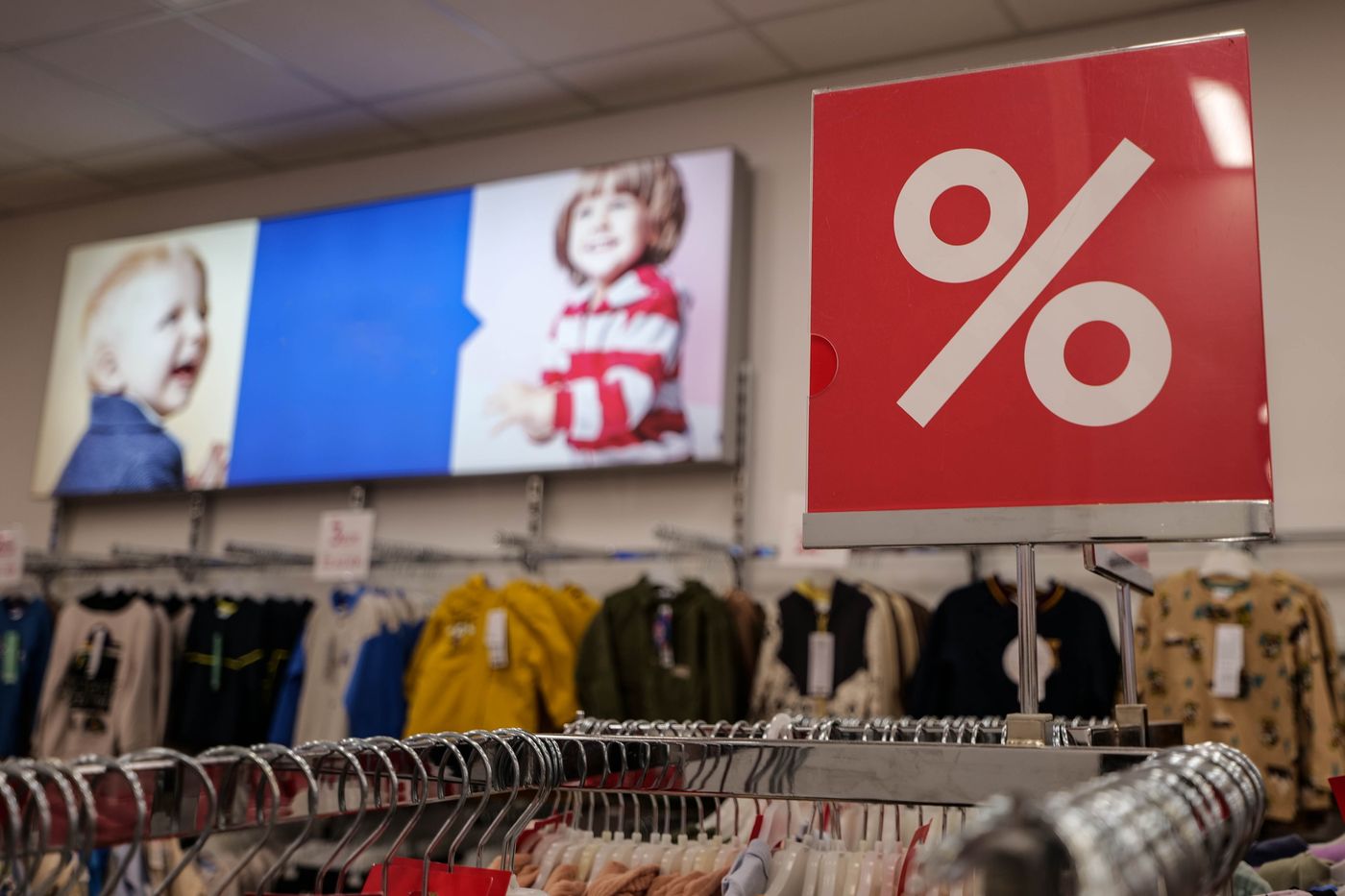 A red percent-sign sale sign standing above racks of children's clothing in a store