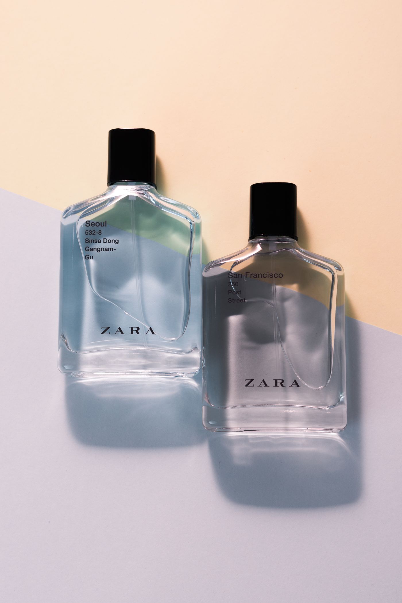 Two Zara fragrance bottles with black caps, labeled Seoul and San Francisco, lying on a split pastel background
