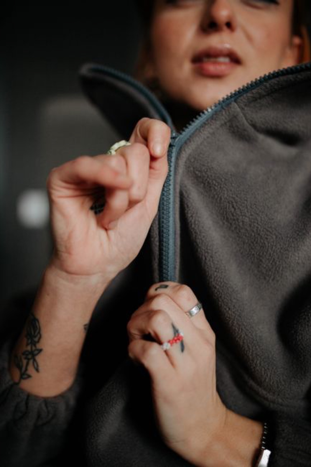 Close-up of hands pulling the zipper of a gray half-zip fleece pullover, brushed pile visible around the collar
