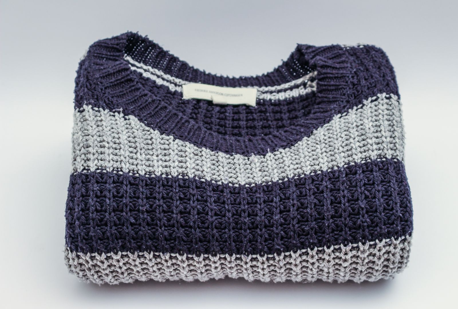 Folded navy and gray striped chunky knit crewneck sweater with a woven brand label visible at the collar