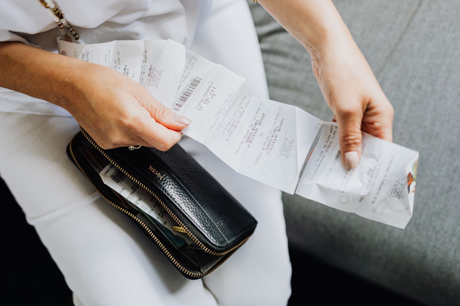 Close-up of two hands fanning several printed till receipts out of a black zip wallet