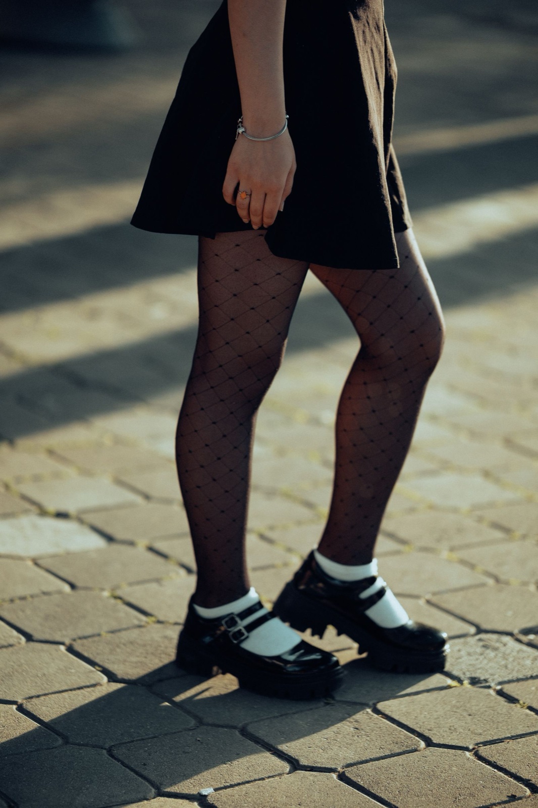 Chunky lug-sole patent mary janes with double straps, worn with white socks and dotted tights on a paved street in low sun