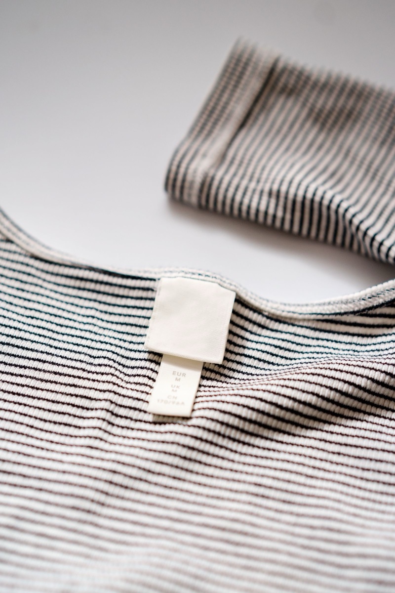 Close-up of a folded striped knit top with a plain white neck label showing EUR, UK and CN sizing