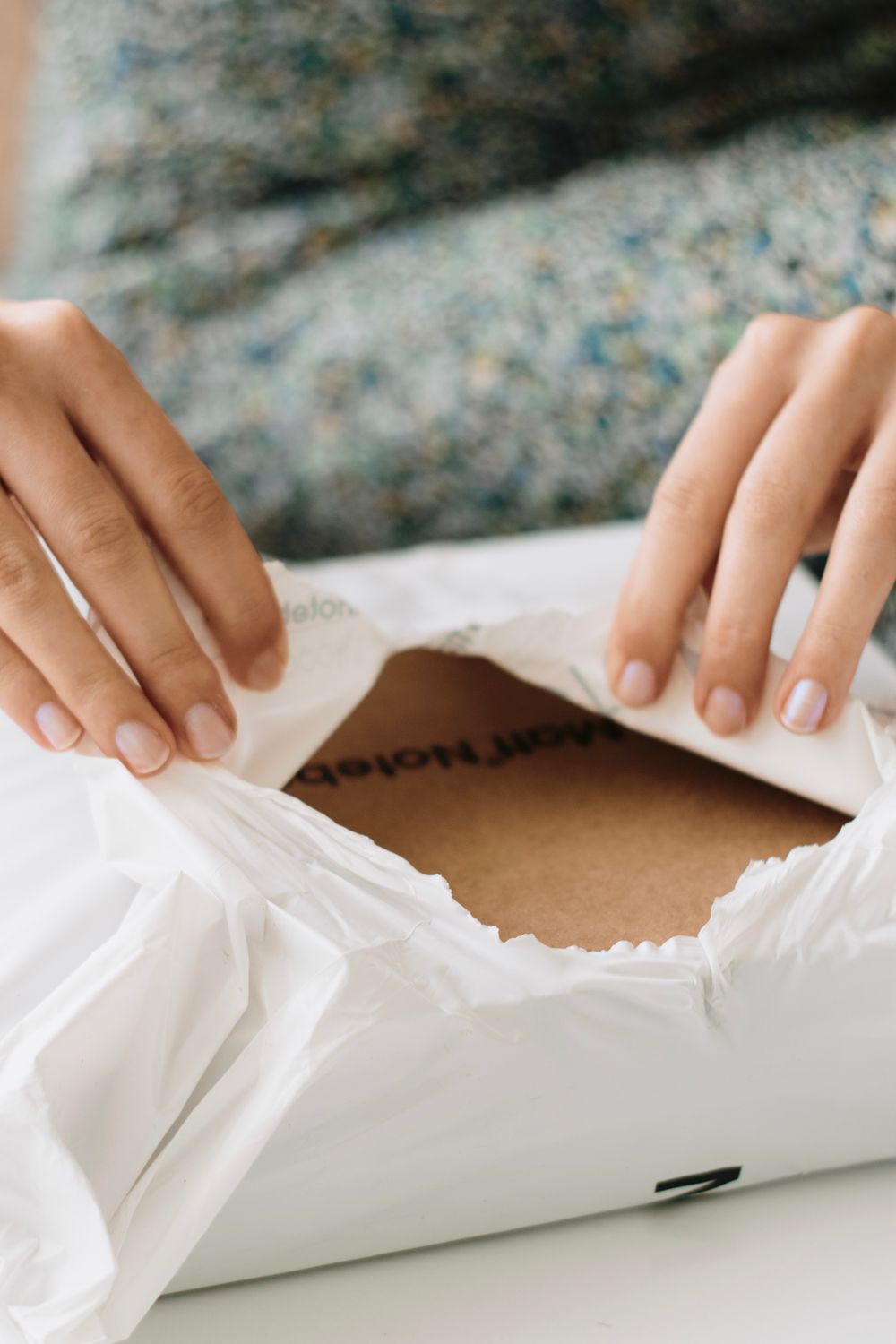 Two hands tearing open a white postal mailer to reveal cardboard packaging inside