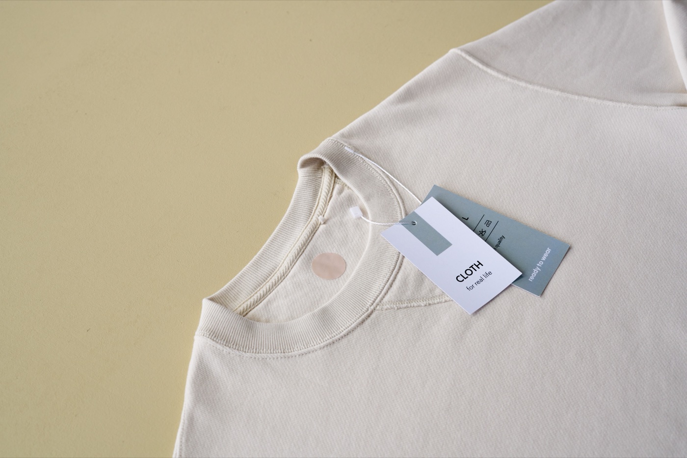 A cream crew-neck top on a brown table with two hang tags attached at the collar, the grey one printed with laundry care symbols