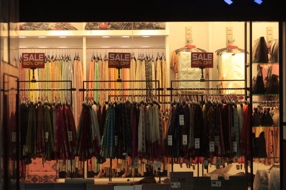 A lit shop window at night with racks of clothing under three signs reading sale 60% off, 50% off and 40% off
