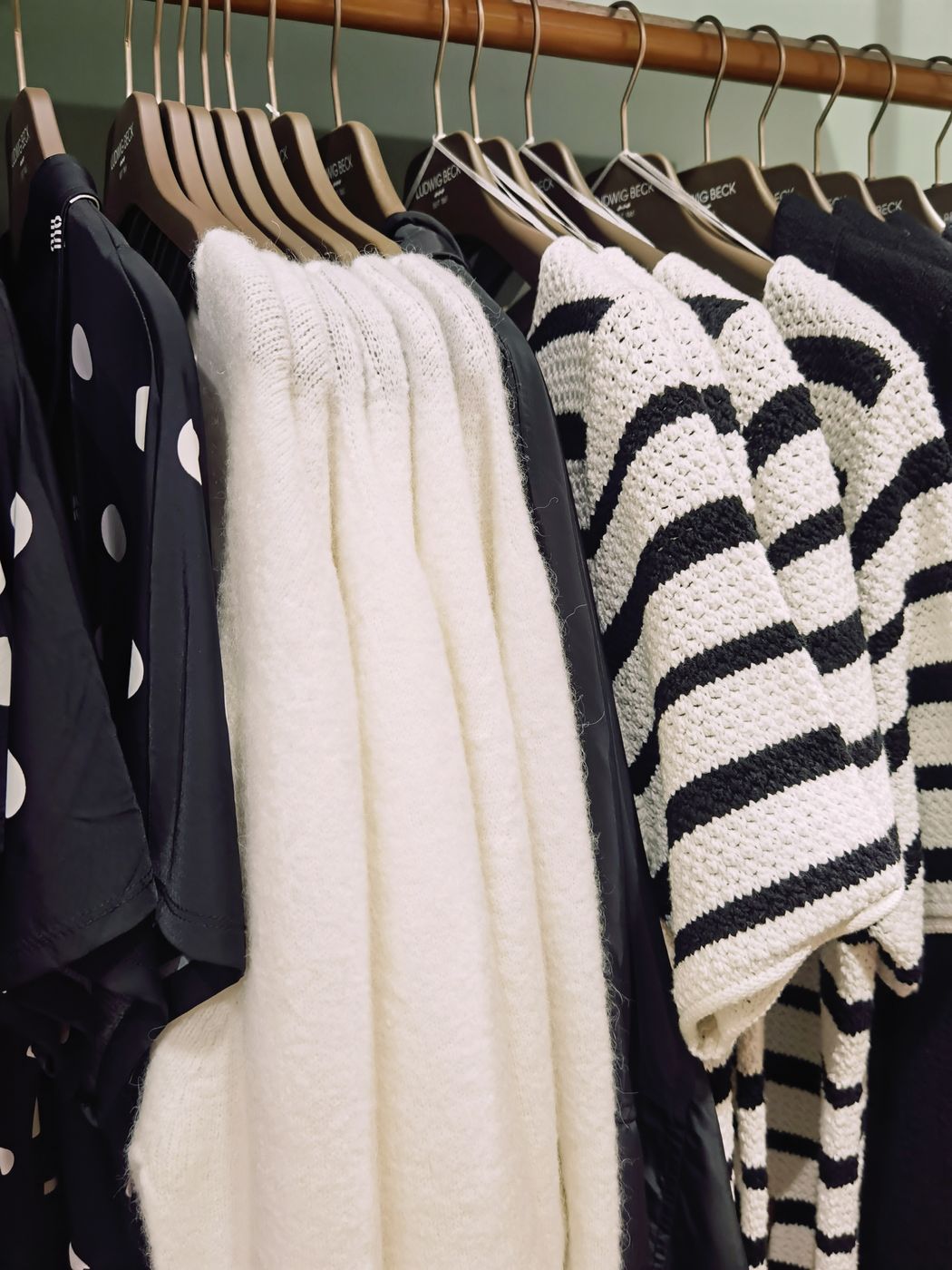 Sweaters and blouses in cream, navy and polka dot patterns hanging on wooden hangers along a boutique rail