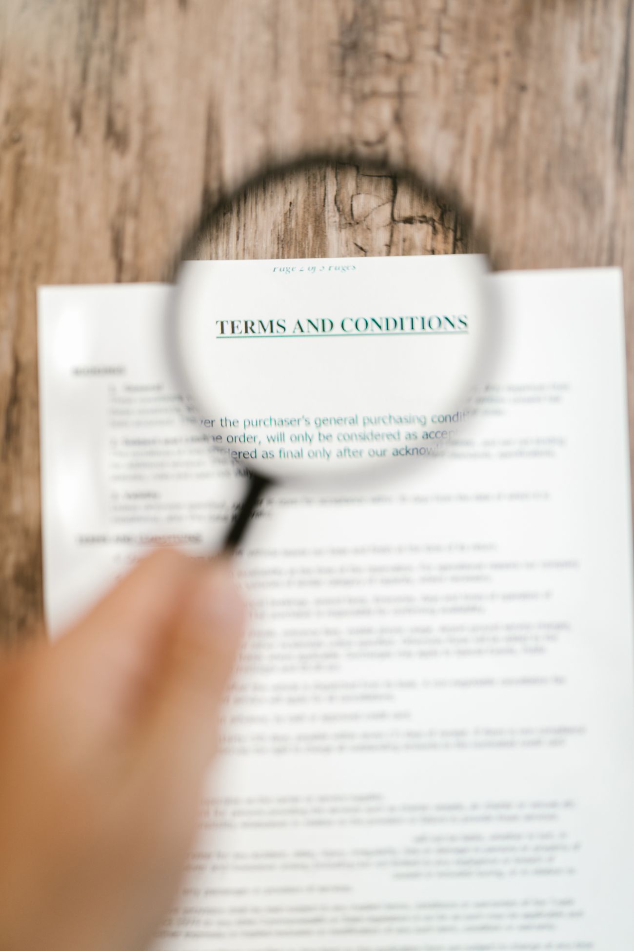 A hand holding a magnifying glass over a printed page headed Terms and Conditions on a wooden table