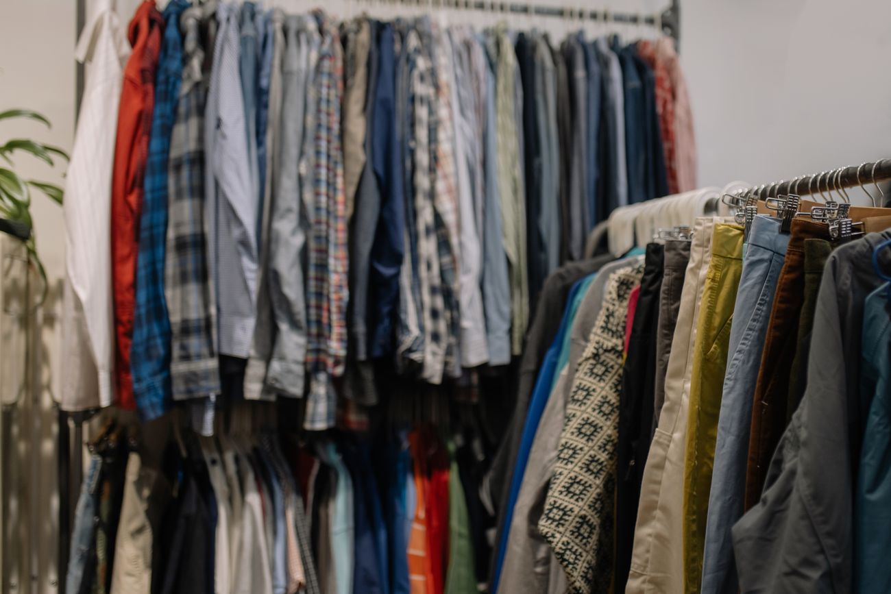 Racks of assorted secondhand shirts and trousers crowded together in a resale shop, shot with a shallow depth of field