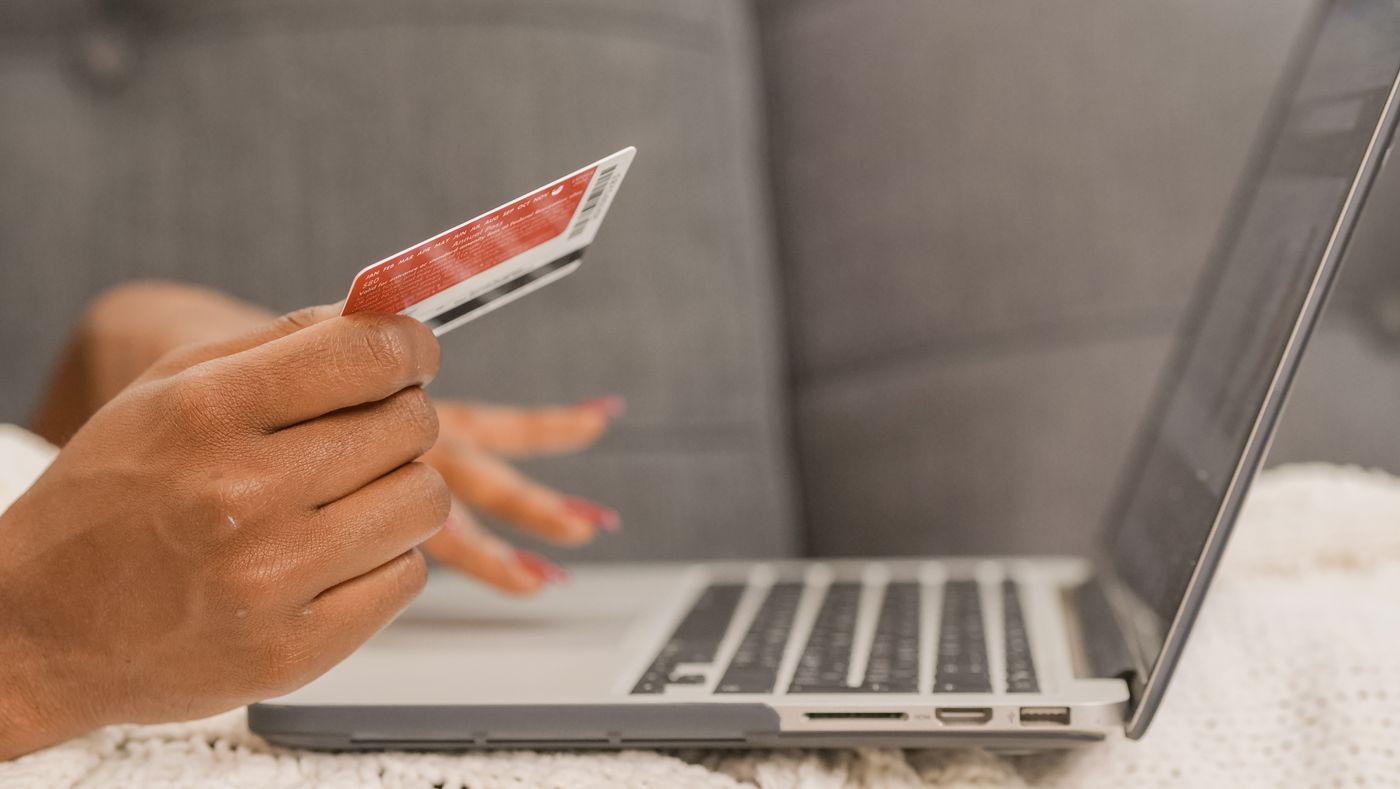 A hand holding a red loyalty card in front of an open laptop on a white knit blanket