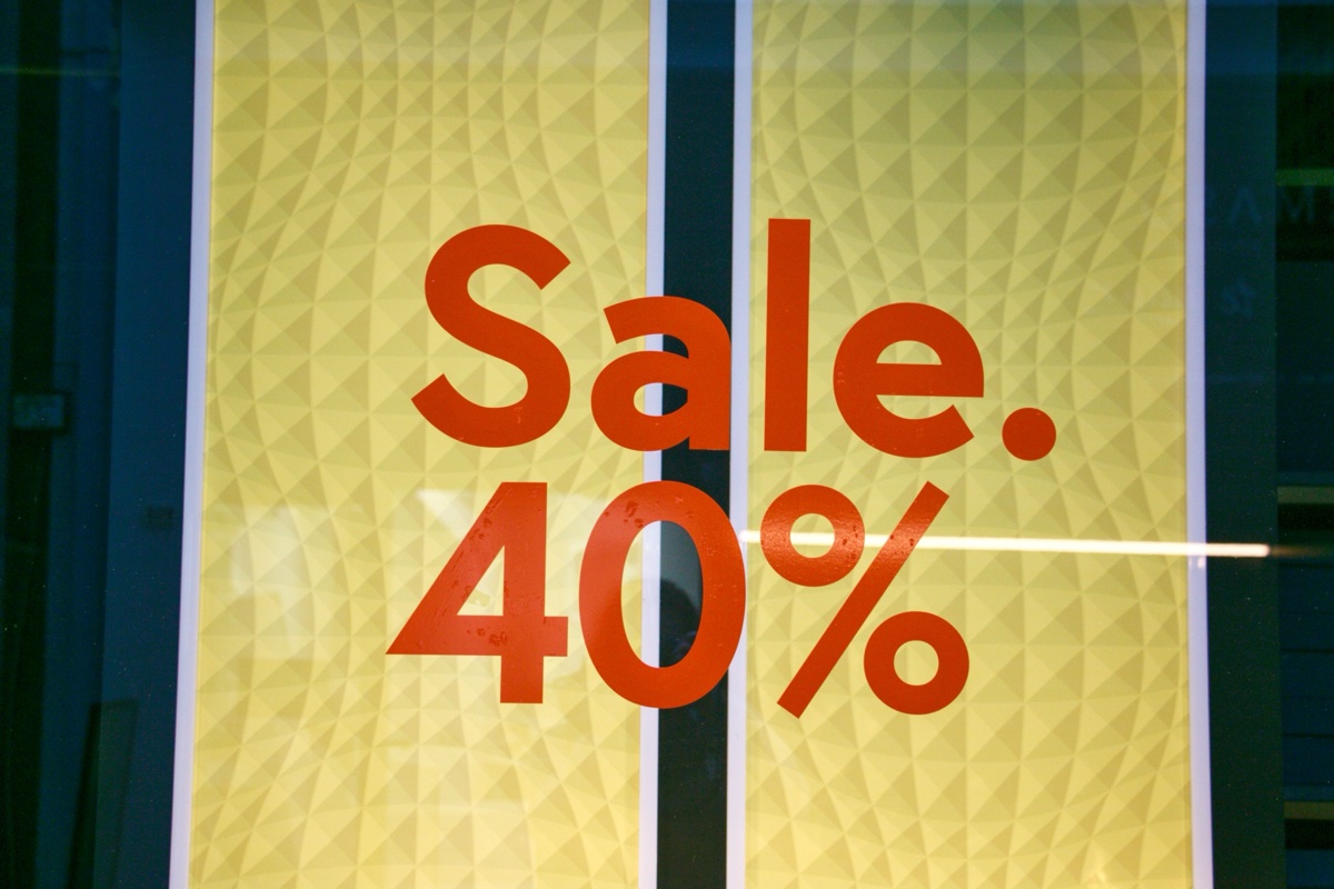 A store window with two yellow posters reading Sale 40 percent in red letters, photographed from the street