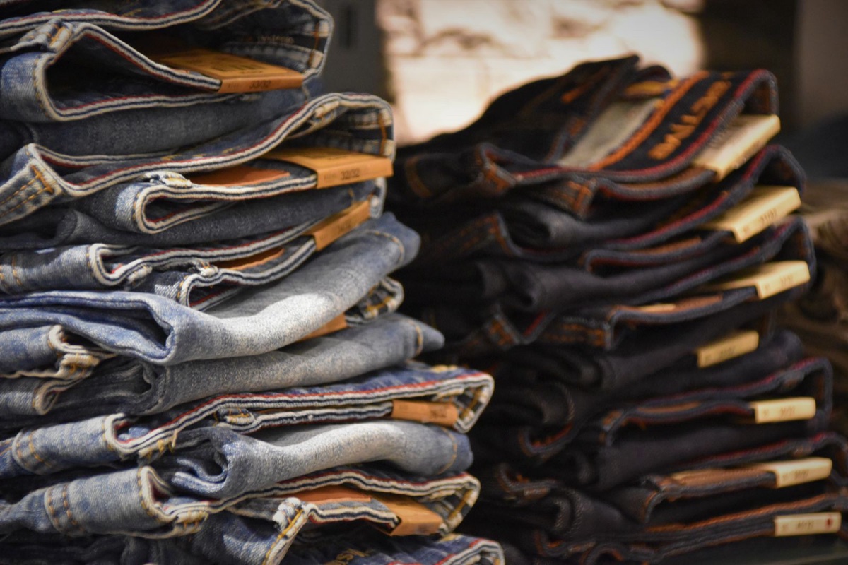 Two tall stacks of folded jeans in a shop, waistband tabs printed with sizes like 33/32 facing out