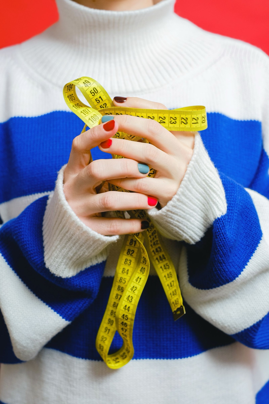 A person in a blue and white striped sweater holding a tangled yellow measuring tape in both hands