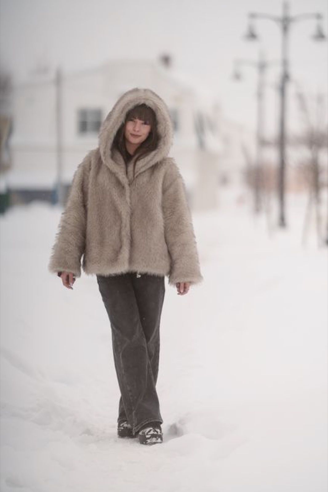 A person in an oversized greige hooded pile coat walking down a snow-covered street