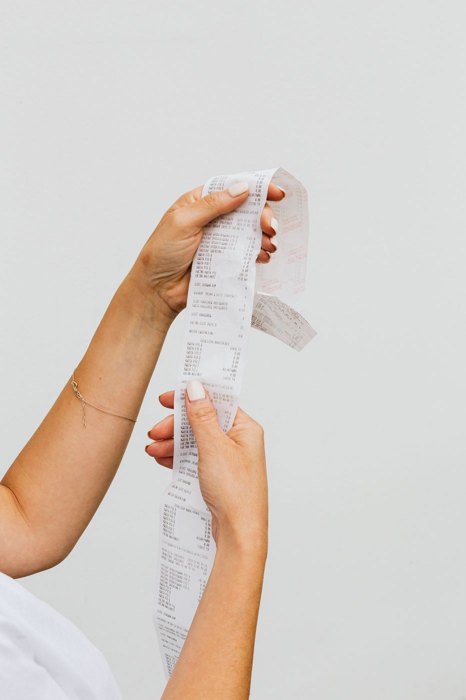 A woman's hands unspooling a long paper till receipt against a plain white background