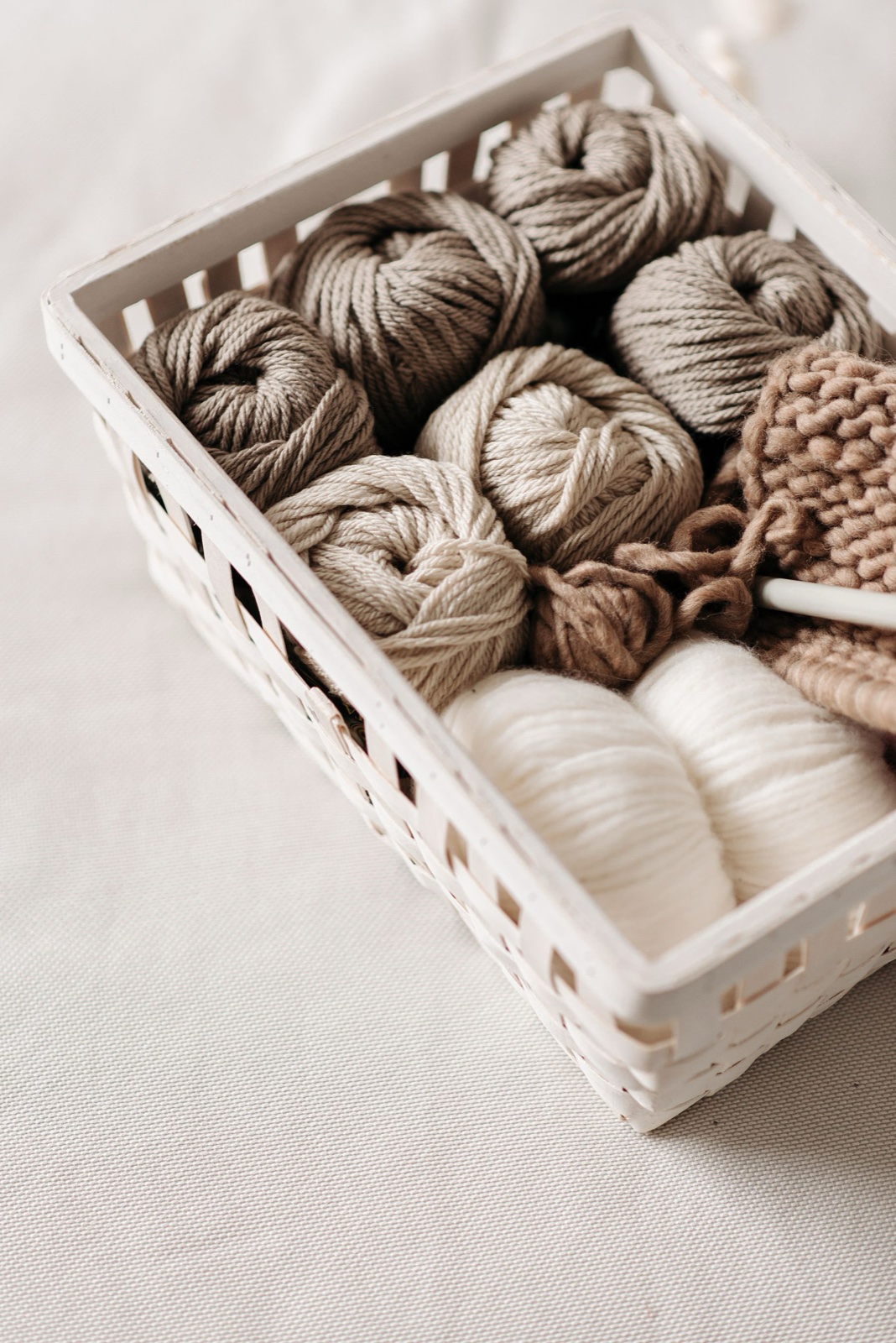 Balls of cream, oatmeal and brown wool yarn packed into a white slatted basket